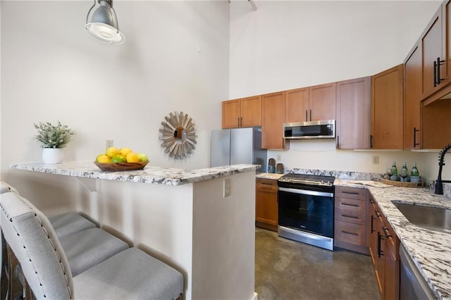 kitchen with light stone counters, a breakfast bar area, a high ceiling, a sink, and appliances with stainless steel finishes