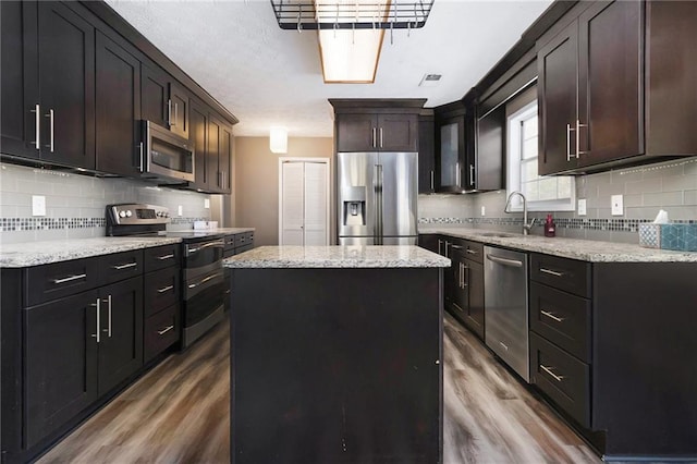 kitchen featuring decorative backsplash, a kitchen island, appliances with stainless steel finishes, wood finished floors, and a sink