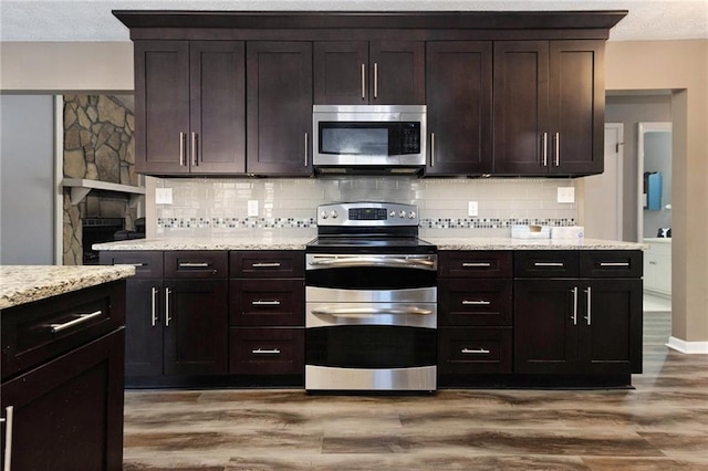 kitchen with stainless steel appliances, light stone counters, light wood-type flooring, and decorative backsplash