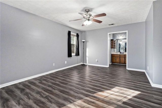 unfurnished bedroom featuring a textured ceiling, dark wood finished floors, visible vents, baseboards, and ensuite bath