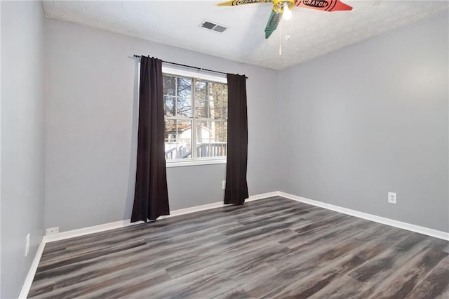 empty room with visible vents, dark wood finished floors, a textured ceiling, and baseboards