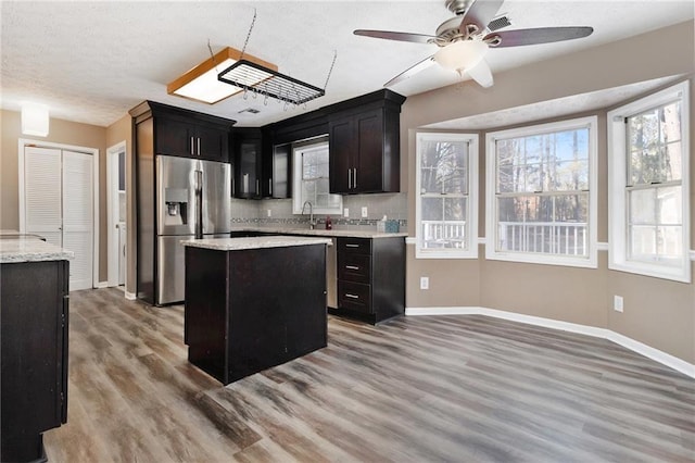 kitchen with light wood-style flooring, a sink, a kitchen island, baseboards, and stainless steel refrigerator with ice dispenser