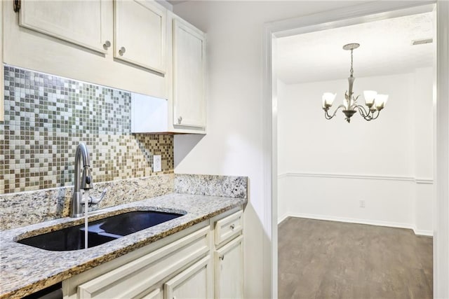 kitchen featuring light stone counters, a chandelier, pendant lighting, tasteful backsplash, and sink