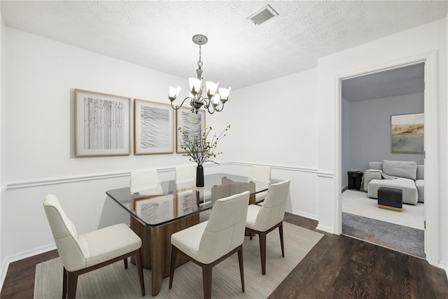 dining area with a textured ceiling, dark wood-type flooring, and a notable chandelier