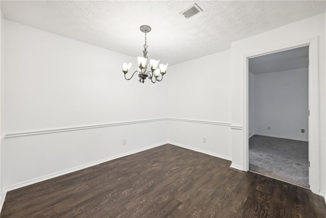 empty room featuring a textured ceiling, a notable chandelier, and dark wood-type flooring