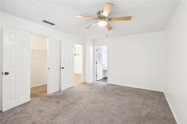 unfurnished bedroom with a closet, ensuite bath, ceiling fan, carpet flooring, and a walk in closet