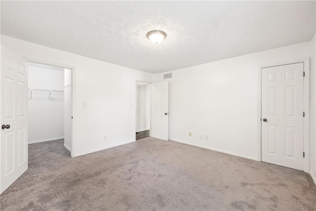 unfurnished bedroom with a closet, a walk in closet, carpet floors, and a textured ceiling