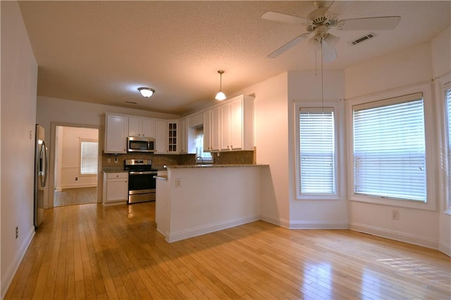 kitchen featuring decorative light fixtures, light wood-type flooring, stainless steel appliances, and white cabinetry