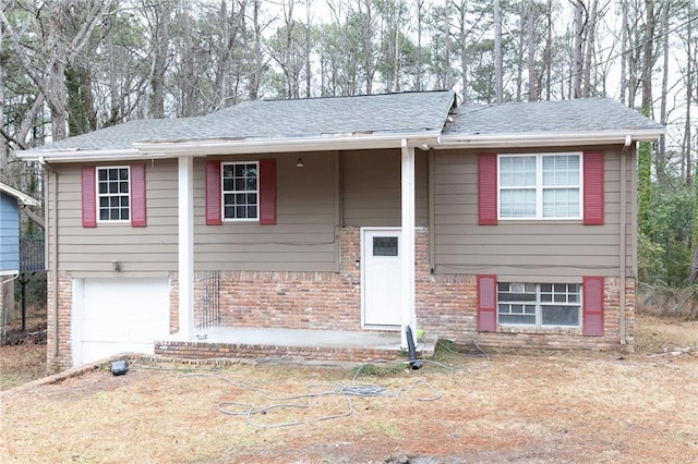 raised ranch featuring a shingled roof, brick siding, and an attached garage