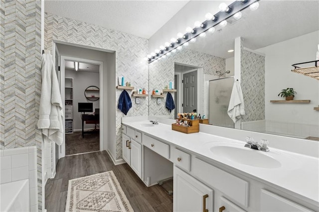 bathroom with a stall shower, a sink, a textured ceiling, and wallpapered walls