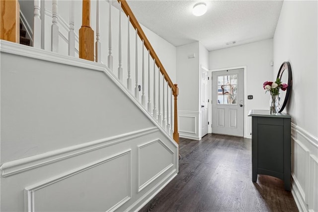 entrance foyer featuring visible vents, dark wood finished floors, stairway, a textured ceiling, and a decorative wall