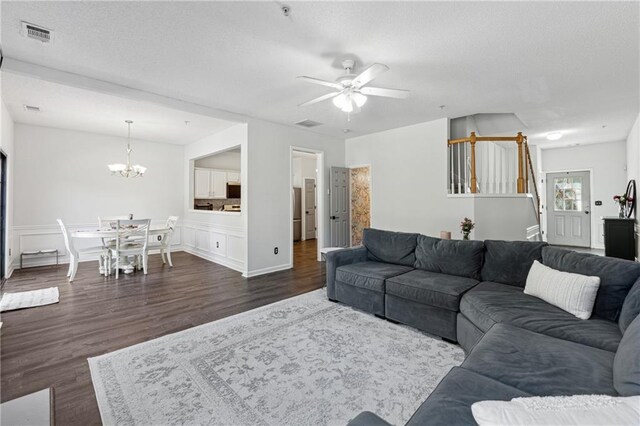 living area with stairway, visible vents, dark wood-style flooring, and ceiling fan with notable chandelier