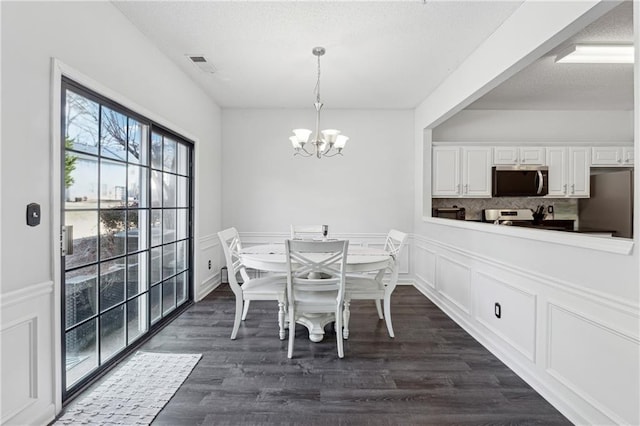 dining room featuring visible vents, dark wood-style floors, a wainscoted wall, a chandelier, and a decorative wall