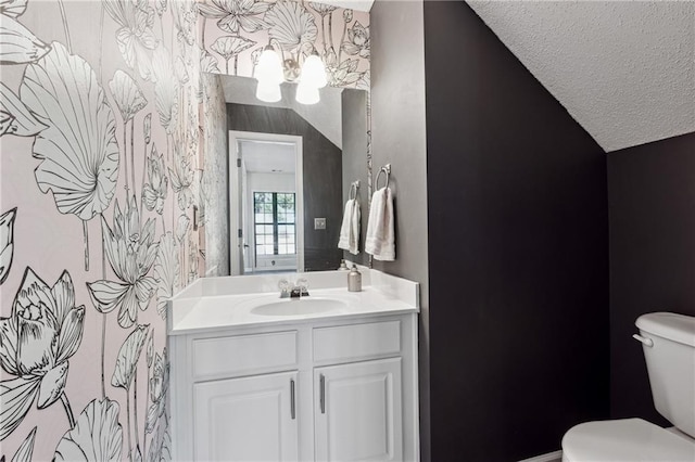 half bath featuring a textured ceiling, vanity, toilet, and wallpapered walls