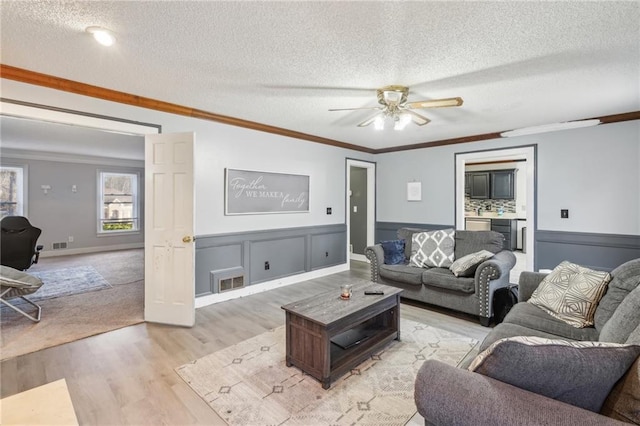 living room with ceiling fan, crown molding, light hardwood / wood-style floors, and a textured ceiling