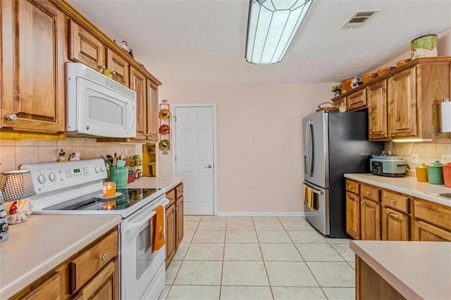 kitchen featuring light tile patterned floors, white appliances, brown cabinetry, and visible vents