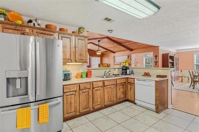 kitchen featuring a peninsula, a sink, visible vents, dishwasher, and stainless steel fridge