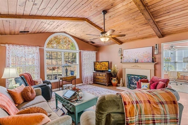 living area with vaulted ceiling with beams, a fireplace with raised hearth, plenty of natural light, and a ceiling fan