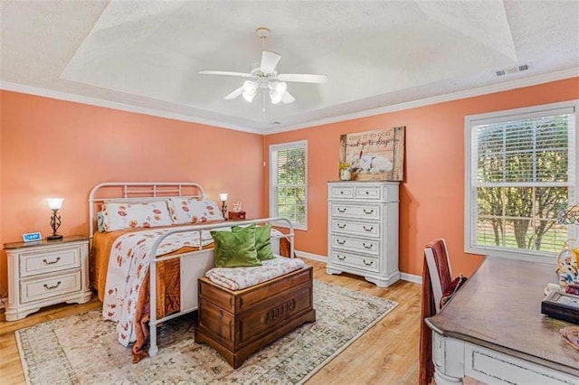 bedroom with ornamental molding, a tray ceiling, wood finished floors, and visible vents