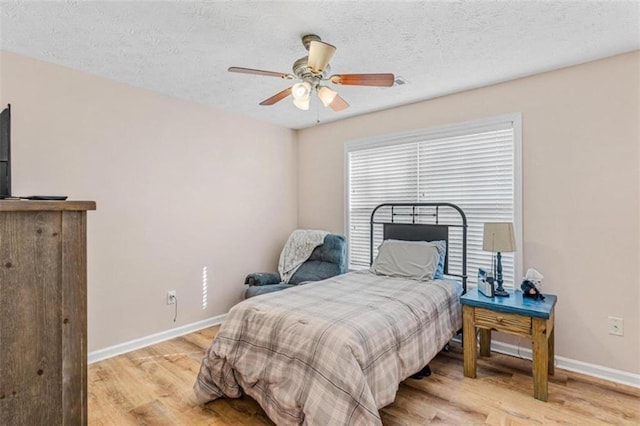 bedroom with light wood-style floors, a textured ceiling, baseboards, and a ceiling fan