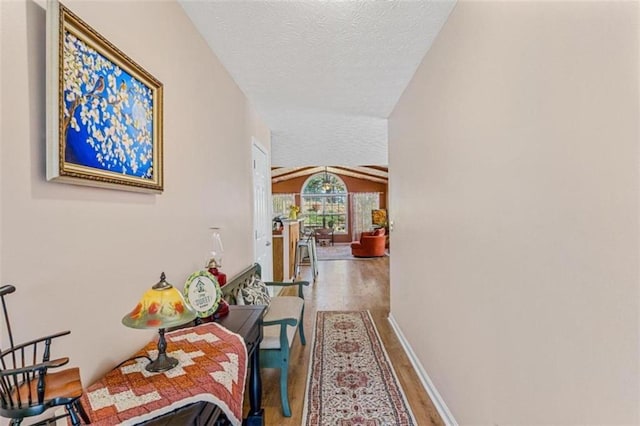 corridor featuring vaulted ceiling, a textured ceiling, baseboards, and wood finished floors