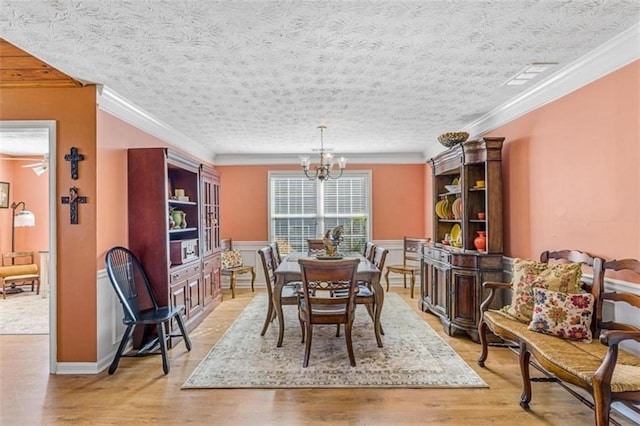 dining area featuring light wood-type flooring, an inviting chandelier, ornamental molding, and a textured ceiling