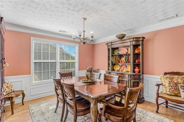 dining area with a textured ceiling, light wood-type flooring, visible vents, and an inviting chandelier