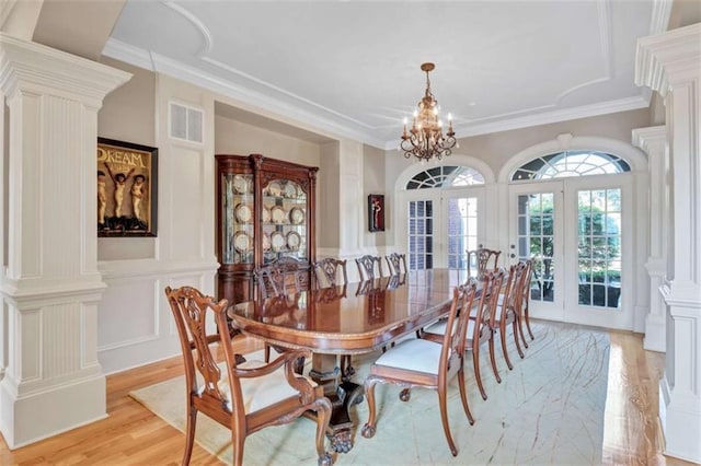 dining area with french doors, decorative columns, a decorative wall, light wood-style floors, and a chandelier