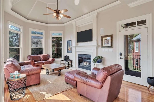 interior space featuring a glass covered fireplace, a towering ceiling, ceiling fan, crown molding, and light wood-style floors