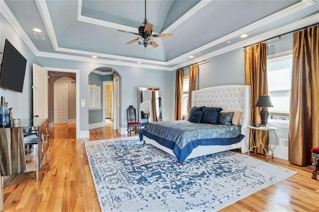 bedroom featuring arched walkways, baseboards, light wood finished floors, ornamental molding, and a tray ceiling