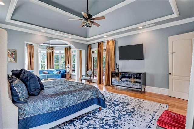 bedroom with baseboards, arched walkways, a raised ceiling, ornamental molding, and wood finished floors