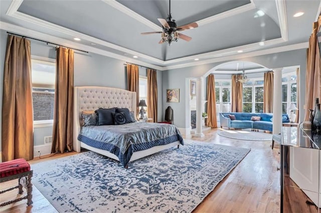 bedroom featuring a tray ceiling, multiple windows, decorative columns, and arched walkways