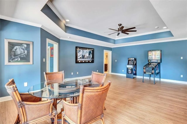 dining room with a tray ceiling, light wood-style floors, ornamental molding, ceiling fan, and baseboards