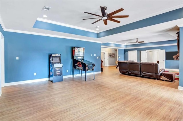 living room with visible vents, baseboards, light wood-style flooring, a tray ceiling, and crown molding