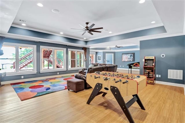 recreation room with a raised ceiling, visible vents, light wood-style floors, ornamental molding, and baseboards