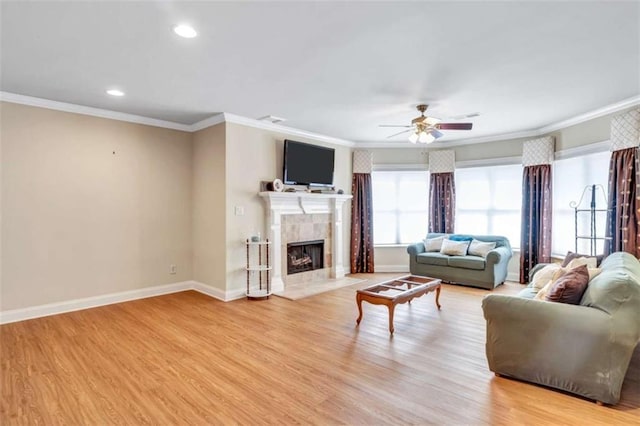 living room featuring baseboards, a tiled fireplace, a ceiling fan, and light wood-style floors