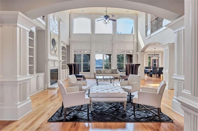 living room with plenty of natural light, arched walkways, a glass covered fireplace, light wood-style floors, and built in shelves