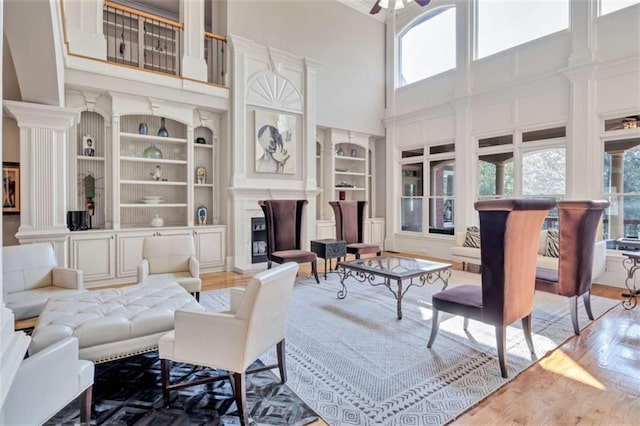 living room featuring built in features, a fireplace, ceiling fan, and wood finished floors