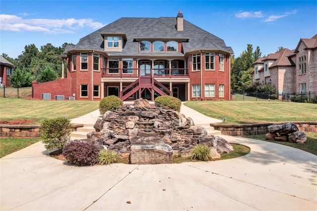 view of front facade featuring brick siding, stairs, fence, and a front yard