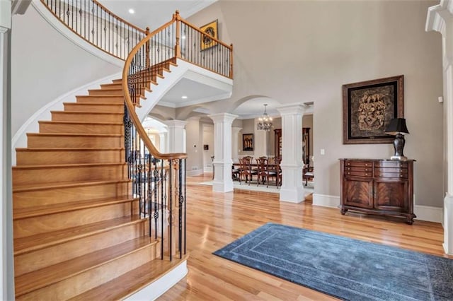 foyer entrance featuring ornate columns, arched walkways, light wood finished floors, and ornamental molding