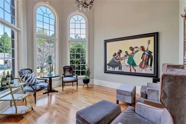 sitting room featuring a notable chandelier, a towering ceiling, baseboards, and wood finished floors