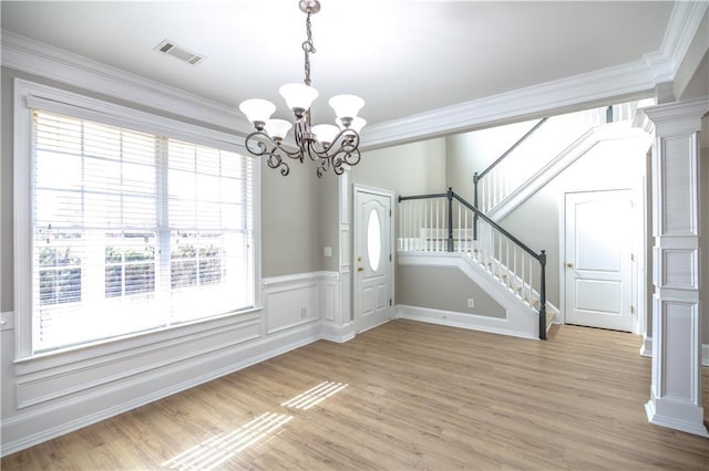 unfurnished dining area with light wood-type flooring, an inviting chandelier, ornamental molding, and ornate columns