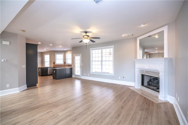 unfurnished living room featuring light hardwood / wood-style floors, sink, ceiling fan, and a fireplace