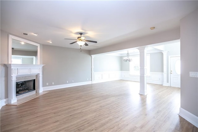 unfurnished living room featuring ceiling fan with notable chandelier, a high end fireplace, decorative columns, and light hardwood / wood-style flooring