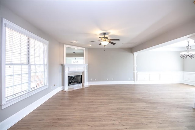 unfurnished living room featuring a premium fireplace, hardwood / wood-style flooring, and ceiling fan with notable chandelier