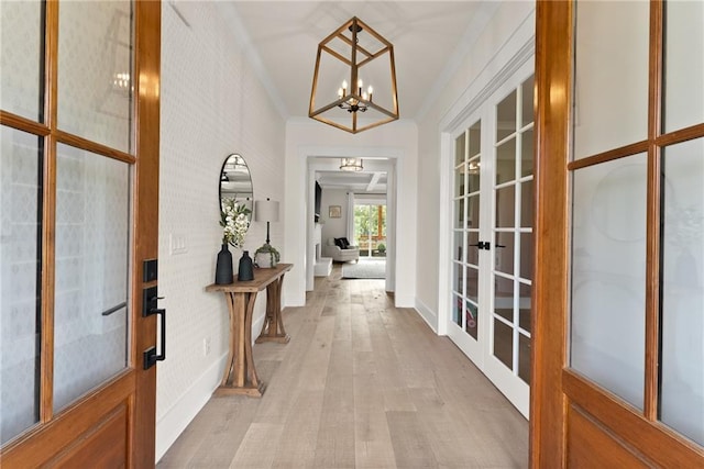 entrance foyer featuring an inviting chandelier, ornamental molding, french doors, and light wood-style floors