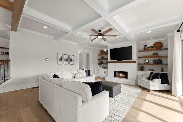 living area with wood finished floors, ceiling fan, a lit fireplace, beamed ceiling, and coffered ceiling