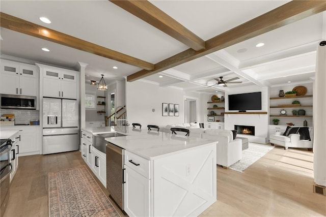 kitchen featuring stainless steel appliances, a sink, beamed ceiling, a warm lit fireplace, and ceiling fan