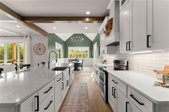 kitchen with a sink, light wood-style floors, a large island, premium range hood, and range with two ovens