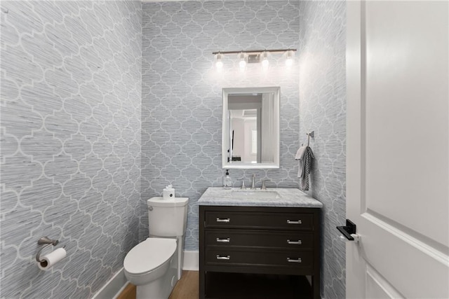 half bath with toilet, vanity, and wood finished floors